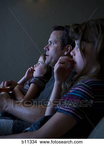 Picture - Father and daughters watching movie in home theater. Fotosearch