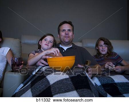 Stock Image - Father and daughters watching movie in home theater. Fotosearch