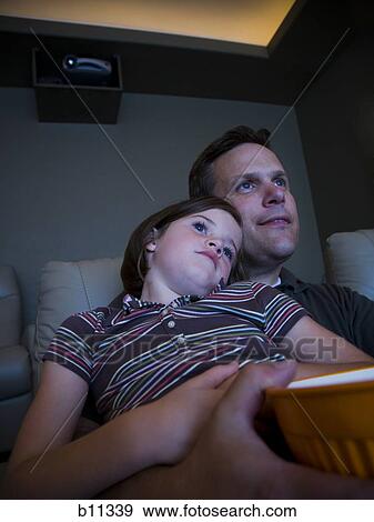 Stock Photo - Father and daughters watching movie in home theater. Fotosearch