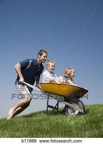 Father pushing son and daughter in a wheelbarrow View Large Photo Image Stock Photograph - Father pushing son and daughter in a wheelbarrow. Fotosearch