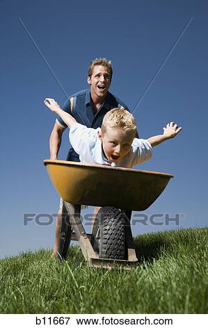 Father pushing son in a wheelbarrow View Large Photo Image Stock Photo - Father pushing son in a wheelbarrow. Fotosearch