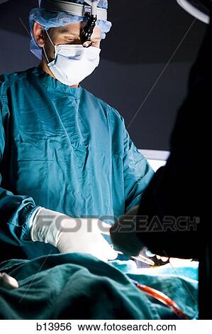 Stock Photograph - Female doctor in scrubs with head light in surgery. Fotosearch