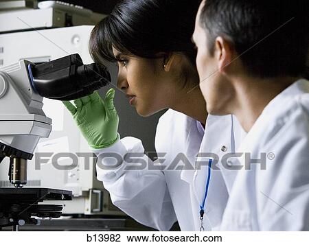 Female lab technician looking through microscope with male technician View Large Photo Image Stock Image - Female lab technician looking through microscope with male technician. Fotosearch