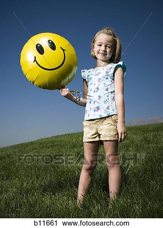 Girl on a hill holding happy face balloon View Large Photo Image Stock Image - Girl on a hill holding happy face balloon. Fotosearch