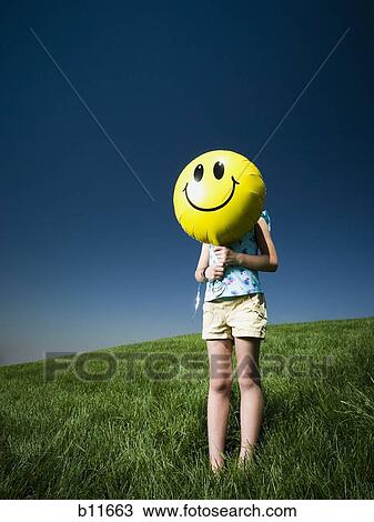 Girl on a hill holding happy face balloon View Large Photo Image Stock Image - Girl on a hill holding happy face balloon. Fotosearch