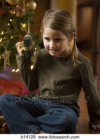 Girl shaking Christmas present with tree View Large Photo Image Stock Photo - Girl shaking Christmas present with tree. Fotosearch