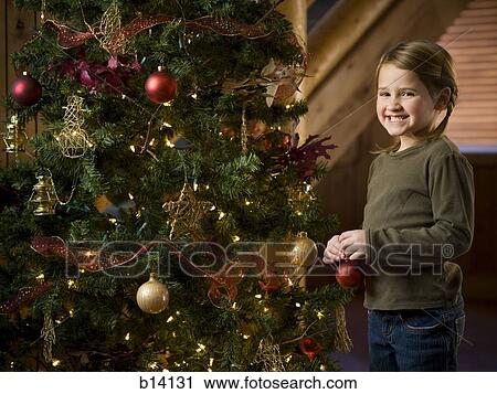Stock Image - Girl with Christmas bauble and Christmas tree. Fotosearch