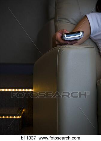 Stock Photo - Hand holding remote control in home theater. Fotosearch