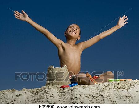 Low angle view of a boy sitting beside a sand castle with his arms outstretched View Large Photo Image Stock Image - Low angle view of a boy sitting beside a sand castle with his arms outstretched. Fotosearch