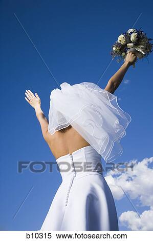 Stock Photography - Low angle view of a bride holding a bouquet of flowers with her arms raised. Fotosearch