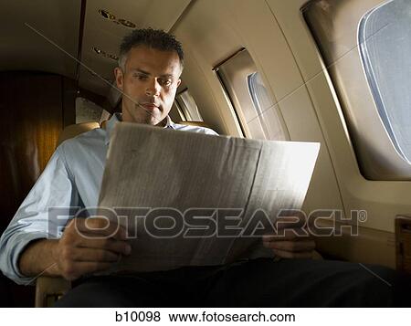 Low angle view of a businessman reading a newspaper in an airplane View Large Photo Image Stock Photo - Low angle view of a businessman reading a newspaper in an airplane. Fotosearch