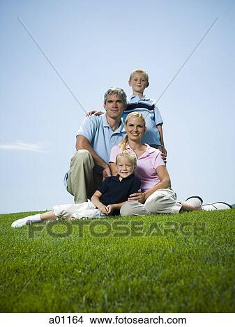 Low angle view of a family sitting on grass View Large Photo Image Picture - Low angle view of a family sitting on grass. Fotosearch