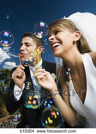 Low angle view of a newlywed couple blowing bubbles with a bubble wand View Large Photo Image Picture - Low angle view of a newlywed couple blowing bubbles with a bubble wand. Fotosearch