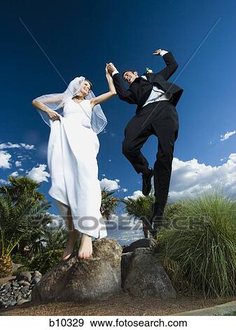 Stock Photo - Low angle view of a newlywed couple holding hands and jumping. Fotosearch