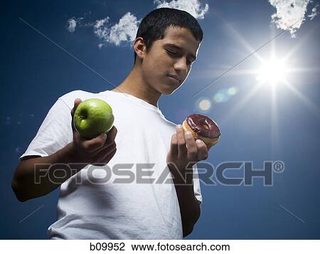 Low angle view of a teenage boy holding an apple and a donut View Large Photo Image Stock Image - Low angle view of a teenage boy holding an apple and a donut. Fotosearch