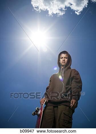 Low angle view of a teenage boy holding a skateboard View Large Photo Image Stock Photo - Low angle view of a teenage boy holding a skateboard. Fotosearch