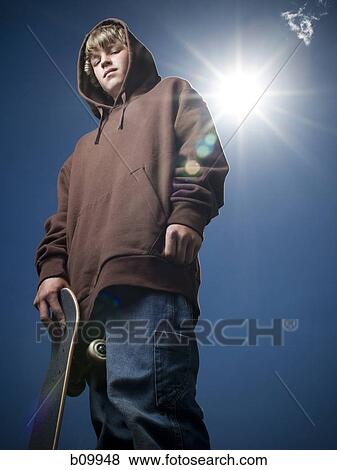 Low angle view of a teenage boy holding a skateboard View Large Photo Image Stock Photo - Low angle view of a teenage boy holding a skateboard. Fotosearch