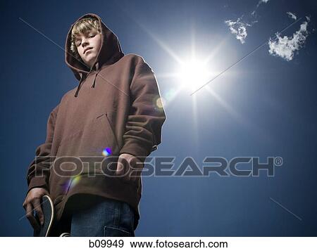 Low angle view of a teenage boy holding a skateboard View Large Photo Image Stock Photo - Low angle view of a teenage boy holding a skateboard. Fotosearch