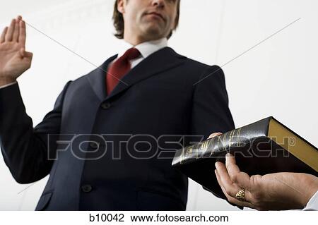 Low angle view of a witness swearing over the Bible View Large Photo Image Stock Image - Low angle view of a witness swearing over the Bible. Fotosearch