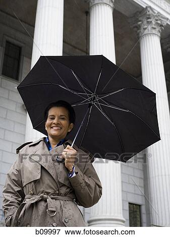 Low angle view of a woman holding an umbrella and smiling View Large Photo Image Stock Photo - Low angle view of a woman holding an umbrella and smiling. Fotosearch