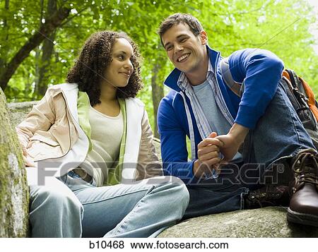 Low angle view of a young couple sitting on a rock View Large Photo Image Stock Photo - Low angle view of a young couple sitting on a rock. Fotosearch