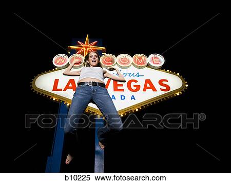 Stock Photography - Low angle view of a young woman jumping in front of a welcome sign, Las Vegas, Nevada, USA. Fotosearch