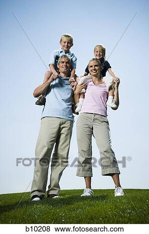 Stock Photo - Low angle view of parents carrying their two children on their shoulders. Fotosearch