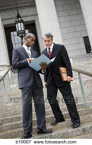 Low angle view of two men looking at documents on the steps of a courthouse View Large Photo Image Stock Photo - Low angle view of two men looking at documents on the steps of a courthouse. Fotosearch