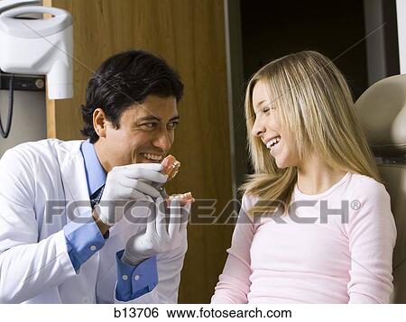 Male dentist holding false teeth talking to girl View Large Photo Image Stock Photograph - Male dentist holding false teeth talking to girl. Fotosearch