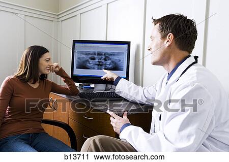 Stock Image - Male doctor or dentist looking at x-rays with woman. Fotosearch