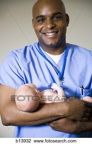 Stock Image - Male nurse or doctor holding newborn baby. Fotosearch