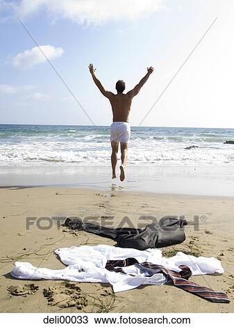 Stock Image - Man in underwear running to water with business attire on sandy beach. Fotosearch