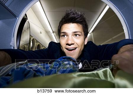 Stock Photo - Man inside dryer at Laundromat with clothing. Fotosearch