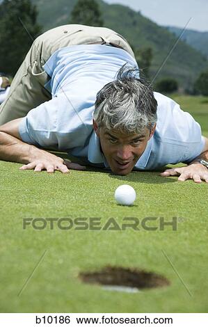 Stock Photograph - Man kneeling near a golf hole. Fotosearch