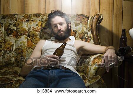 Picture - Man on couch with beer bottle and cigarette. Fotosearch