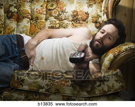 Man on sofa with television remote View Large Photo Image Stock Photography - Man on sofa with television remote. Fotosearch
