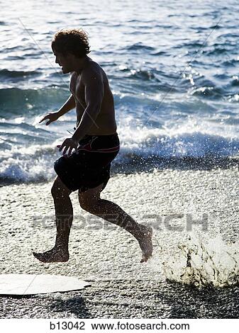 Stock Image - Man running in the surf on a beach. Fotosearch