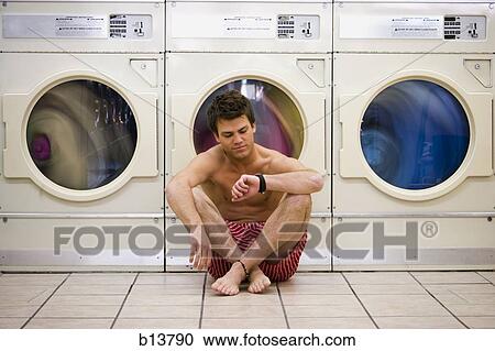 Stock Image - Man sitting in boxers at Laundromat checking watch. Fotosearch