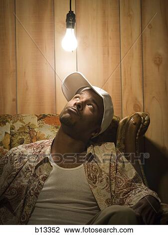 Man sitting on sofa looking up at light bulb View Large Photo Image Stock Image - Man sitting on sofa looking up at light bulb. Fotosearch
