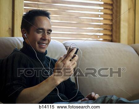 Man sitting on sofa with mp3 player listening to music smiling View Large Photo Image Stock Photography - Man sitting on sofa with mp3 player listening to music smiling. Fotosearch