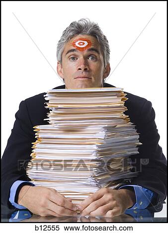 Stock Photography - Man with bull's-eye on forehead with stack of papers. Fotosearch