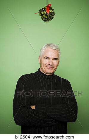 Picture - Man with crossed arms under mistletoe at Christmas. Fotosearch