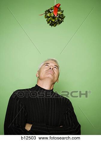 Stock Image - Man with crossed arms under mistletoe at Christmas. Fotosearch