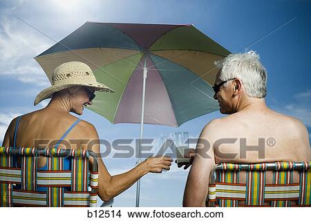 Picture - Mature couple at the beach relaxing on deck chairs. Fotosearch