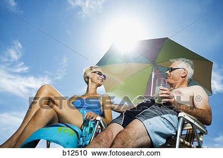 Stock Image - Mature couple at the beach relaxing on deck chairs. Fotosearch