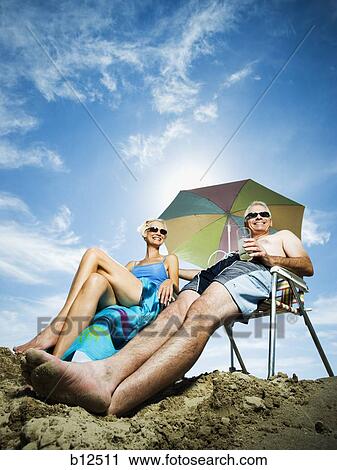 Stock Image - Mature couple at the beach relaxing on deck chairs. Fotosearch
