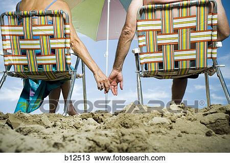 Stock Image - Mature couple at the beach relaxing on deck chairs. Fotosearch
