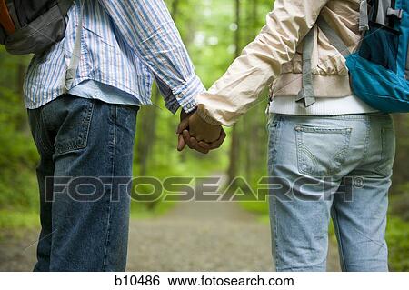 Mid section view of a young couple holding hands and standing View Large Photo Image Stock Photograph - Mid section view of a young couple holding hands and standing. Fotosearch