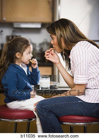 Stock Photography - Mother and young daughter eating cookies. Fotosearch