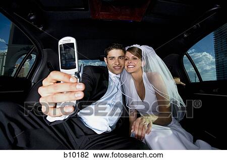 Stock Image - Newlywed couple taking a photograph of themselves with a mobile phone. Fotosearch